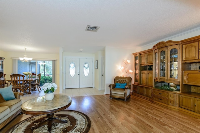 living room with french doors, light hardwood / wood-style floors, a textured ceiling, and a notable chandelier