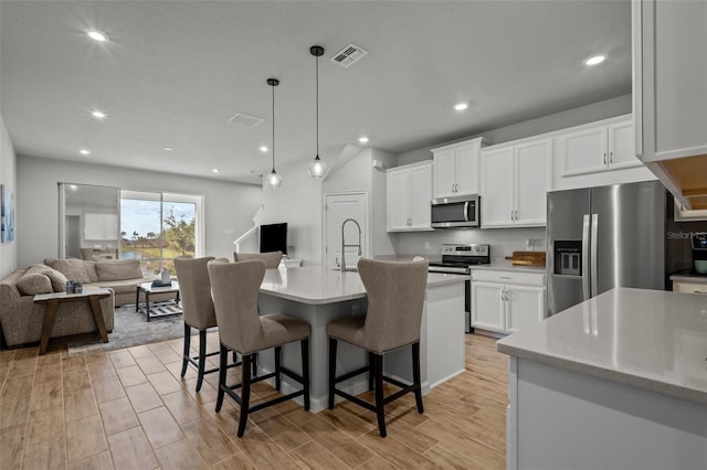 kitchen featuring a center island with sink, light wood-type flooring, pendant lighting, stainless steel appliances, and white cabinets