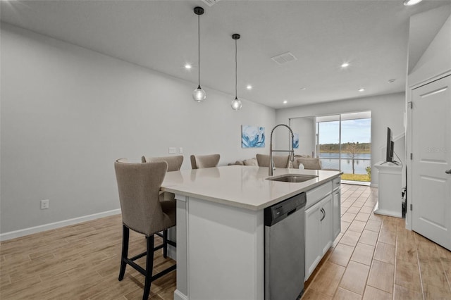 kitchen with white cabinetry, a kitchen island with sink, sink, stainless steel dishwasher, and a breakfast bar area