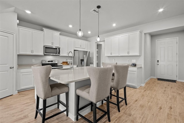 kitchen with a kitchen bar, appliances with stainless steel finishes, a kitchen island with sink, decorative light fixtures, and white cabinets