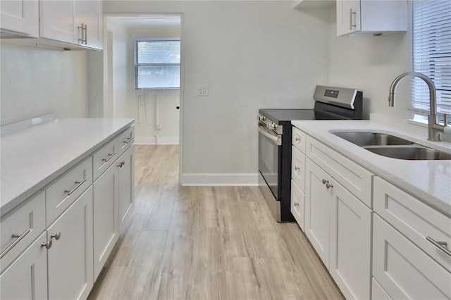 kitchen with stainless steel electric stove, white cabinetry, sink, and light stone countertops