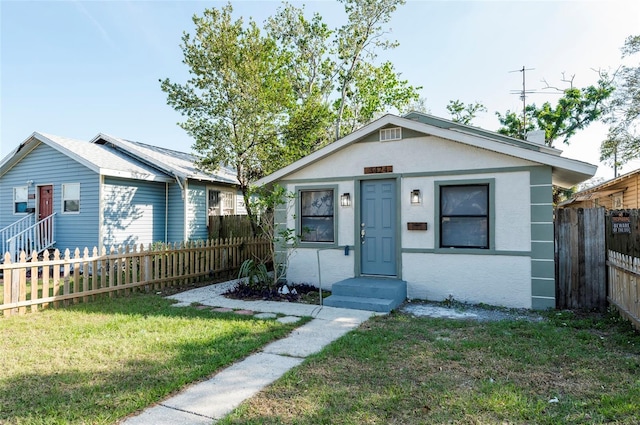 bungalow with fence private yard, stucco siding, and a front yard