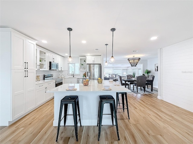 kitchen with white cabinets, appliances with stainless steel finishes, a kitchen island, and hanging light fixtures