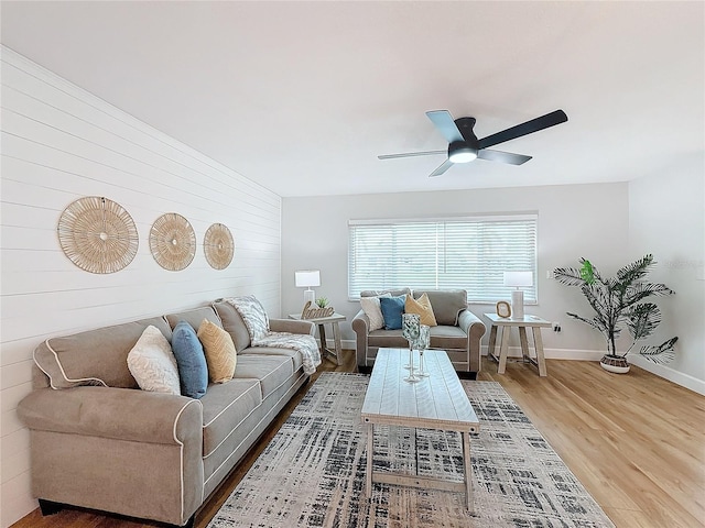 living room featuring wood-type flooring, ceiling fan, and wooden walls