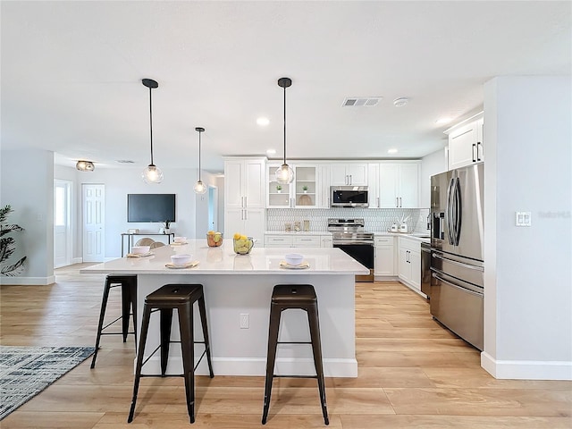 kitchen with a kitchen breakfast bar, backsplash, stainless steel appliances, a kitchen island with sink, and white cabinets