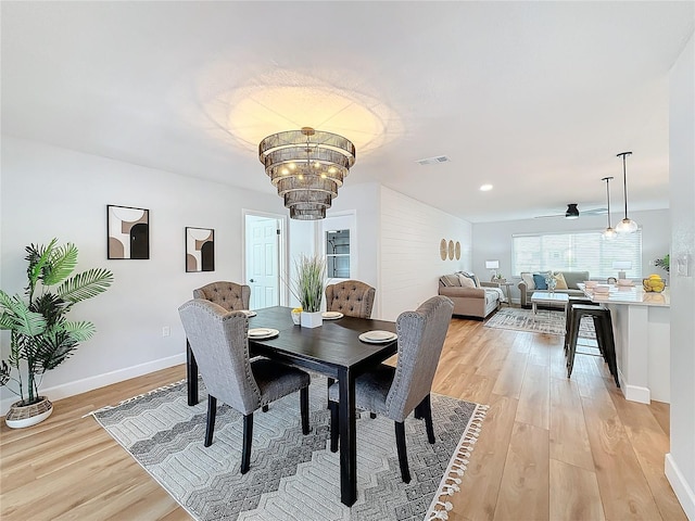 dining space with ceiling fan with notable chandelier and light wood-type flooring