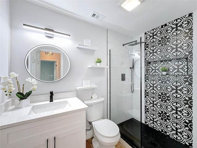 bathroom with tiled shower, vanity, a textured ceiling, and toilet