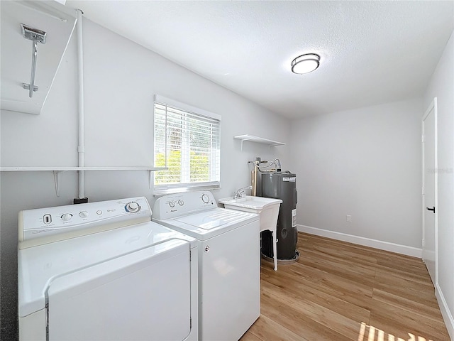 clothes washing area with sink, water heater, a textured ceiling, washer and dryer, and light wood-type flooring