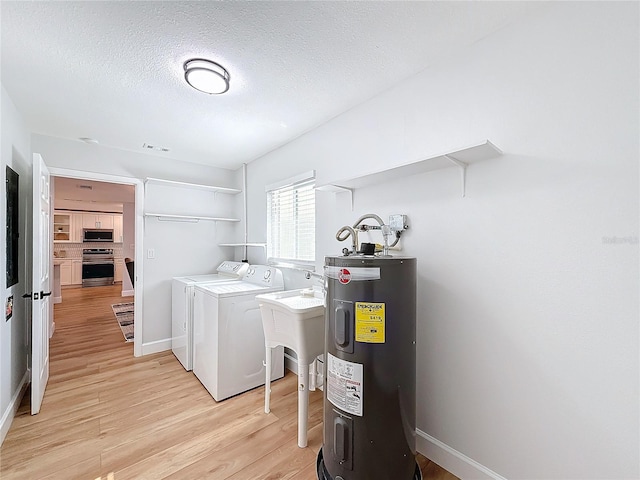 laundry area featuring washer and clothes dryer, electric water heater, a textured ceiling, and light hardwood / wood-style flooring