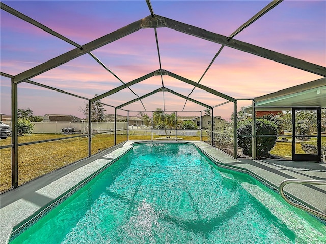 pool at dusk featuring a lanai and a yard