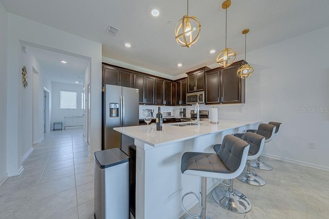 kitchen featuring stainless steel appliances, kitchen peninsula, decorative light fixtures, a kitchen bar, and light tile patterned floors