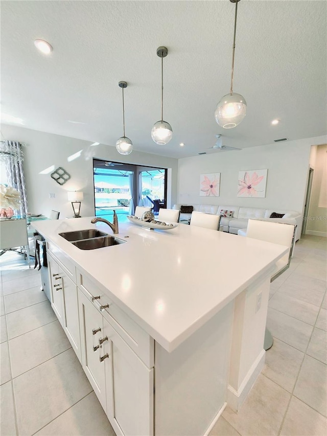 kitchen featuring pendant lighting, sink, white cabinetry, an island with sink, and a textured ceiling