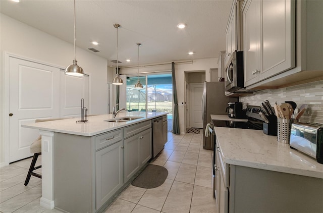 kitchen featuring sink, a kitchen island with sink, stainless steel appliances, decorative light fixtures, and decorative backsplash