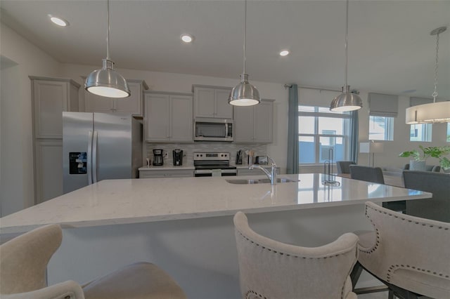 kitchen with backsplash, a large island with sink, a kitchen breakfast bar, hanging light fixtures, and appliances with stainless steel finishes