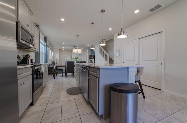 kitchen featuring gray cabinetry, a center island with sink, pendant lighting, and appliances with stainless steel finishes