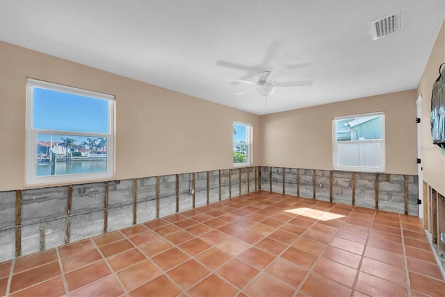 tiled empty room featuring a water view and ceiling fan