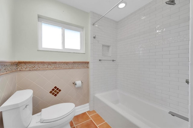 bathroom with tile patterned flooring, tiled shower / bath, toilet, and tile walls