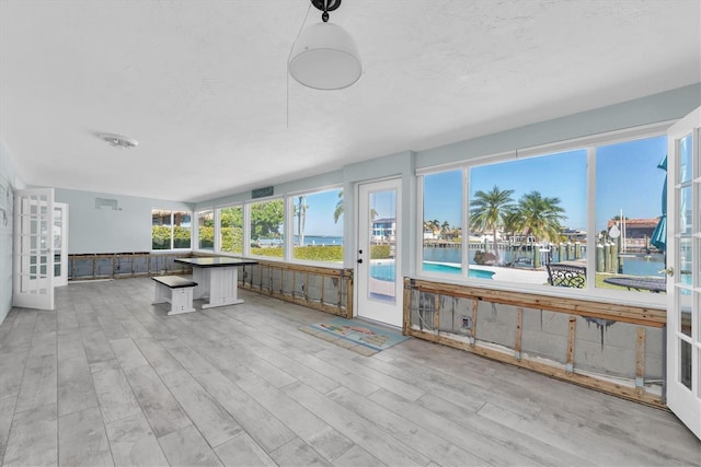 sunroom with a healthy amount of sunlight, a water view, and french doors