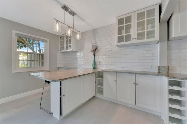 kitchen featuring white cabinetry, kitchen peninsula, pendant lighting, a textured ceiling, and a breakfast bar area