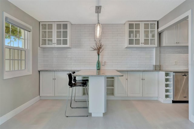 kitchen featuring dishwasher, white cabinets, light stone counters, decorative light fixtures, and a kitchen bar