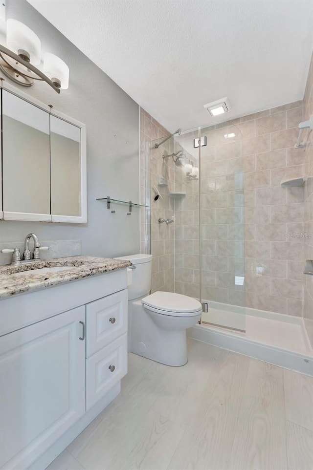 bathroom with a textured ceiling, vanity, toilet, and walk in shower