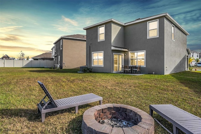 back house at dusk with a patio, an outdoor fire pit, and a lawn