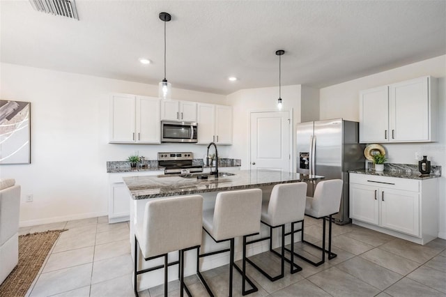 kitchen featuring a center island with sink, sink, appliances with stainless steel finishes, decorative light fixtures, and white cabinetry