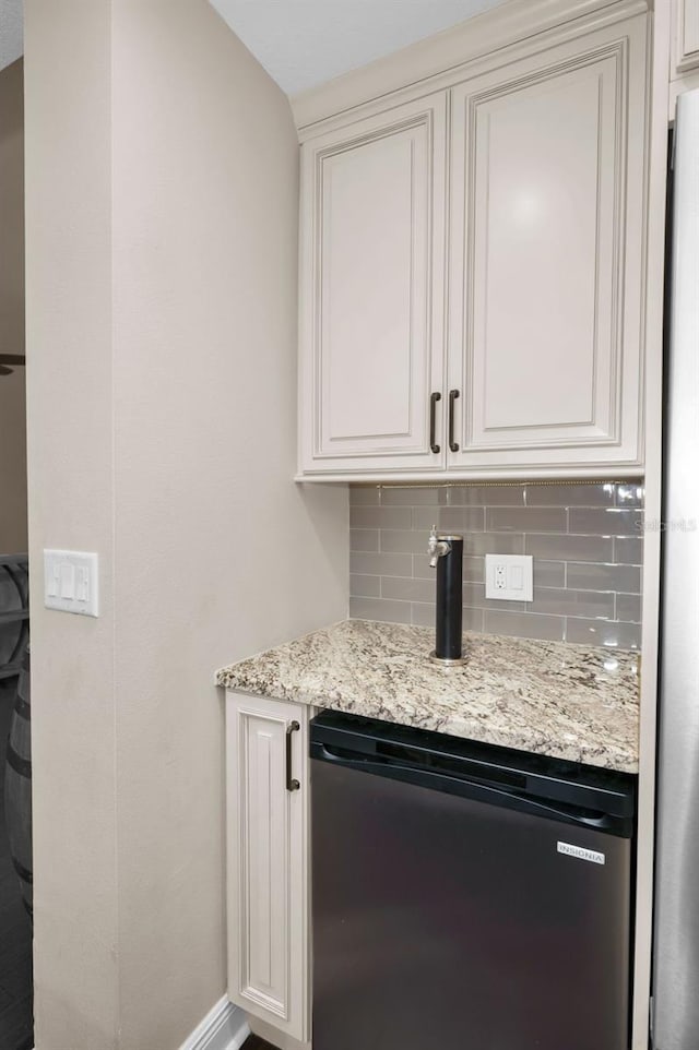 bar with stainless steel refrigerator, backsplash, dishwashing machine, light stone countertops, and white cabinets