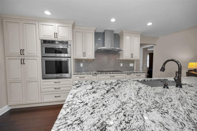 kitchen with wall chimney exhaust hood, sink, light stone counters, black electric cooktop, and stainless steel double oven