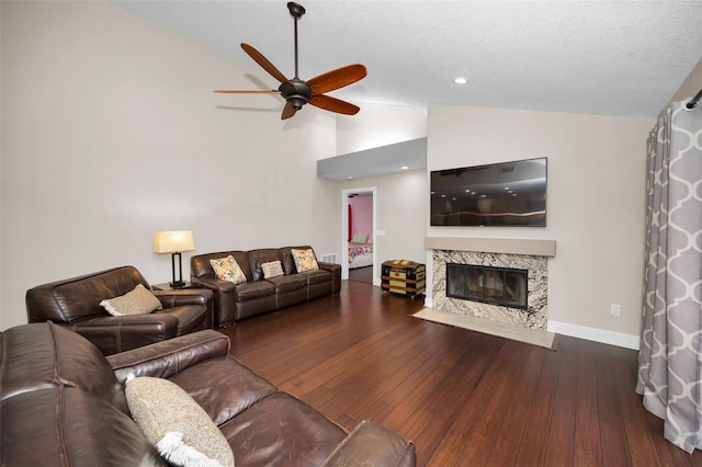 living room featuring dark wood-type flooring, ceiling fan, a premium fireplace, and vaulted ceiling