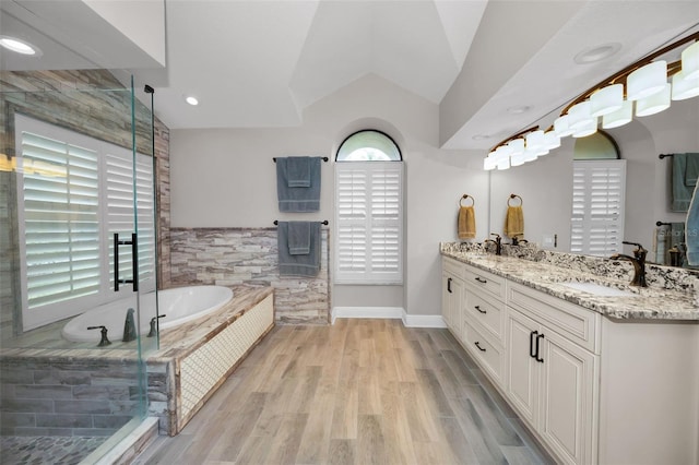 bathroom with wood-type flooring, lofted ceiling, a relaxing tiled tub, and vanity