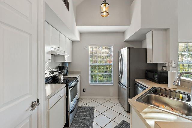 kitchen with white cabinets, sink, light tile patterned floors, appliances with stainless steel finishes, and decorative light fixtures