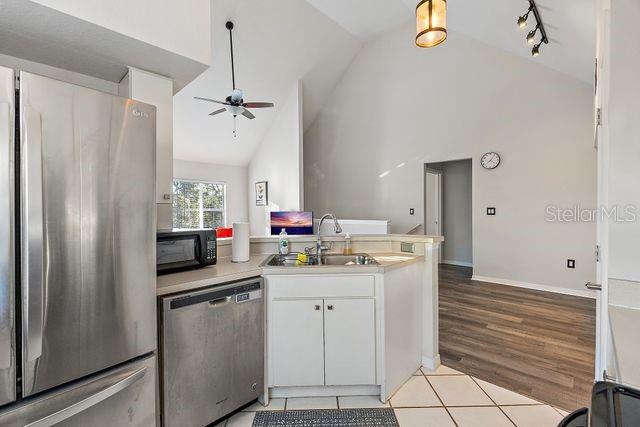 kitchen with appliances with stainless steel finishes, sink, light tile patterned floors, high vaulted ceiling, and white cabinets