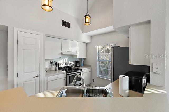 kitchen featuring white cabinets, vaulted ceiling, hanging light fixtures, and electric stove