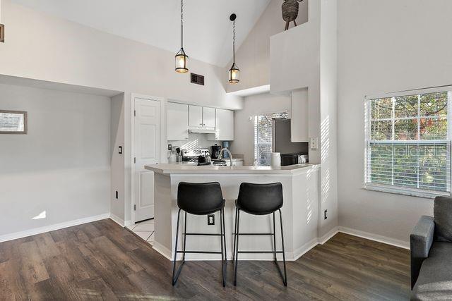 kitchen featuring pendant lighting, high vaulted ceiling, kitchen peninsula, white cabinetry, and a breakfast bar area