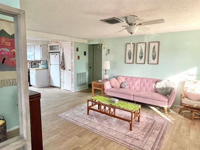 living room featuring ceiling fan, a textured ceiling, and light wood-type flooring