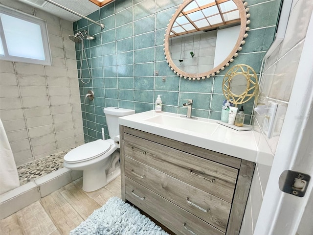 bathroom with vanity, toilet, tile walls, and a tile shower