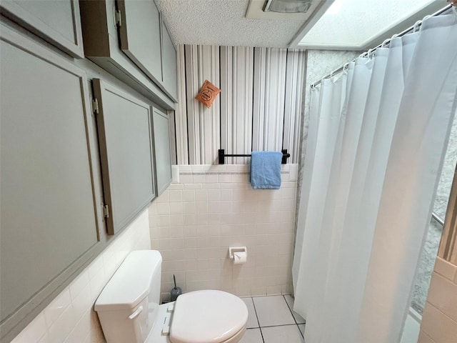 bathroom featuring tile patterned floors, tile walls, a textured ceiling, and toilet