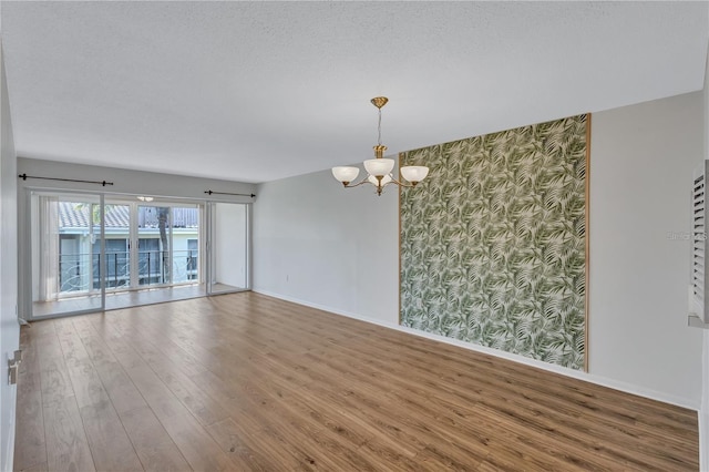 unfurnished room with hardwood / wood-style floors, a textured ceiling, and an inviting chandelier