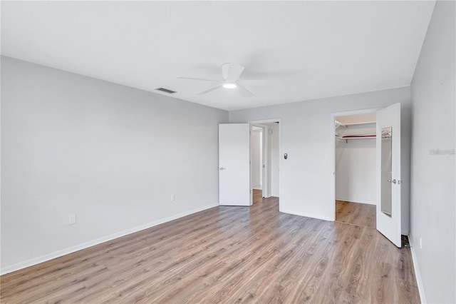 unfurnished bedroom with a walk in closet, ceiling fan, a closet, and light hardwood / wood-style floors