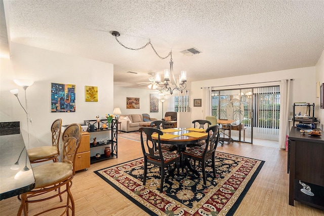 dining space with light wood-type flooring, a textured ceiling, and a notable chandelier