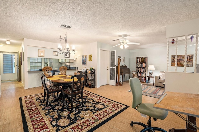 dining space with light hardwood / wood-style flooring, ceiling fan with notable chandelier, and a textured ceiling