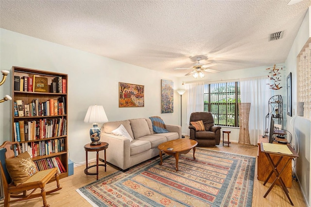 living room featuring ceiling fan, light hardwood / wood-style floors, and a textured ceiling