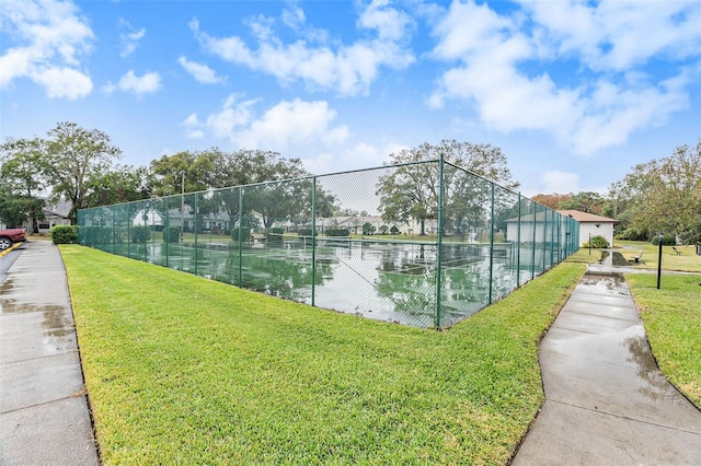 view of tennis court with a water view and a lawn