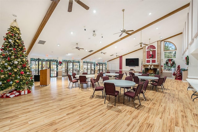 dining room with beamed ceiling, a large fireplace, light hardwood / wood-style flooring, and a healthy amount of sunlight