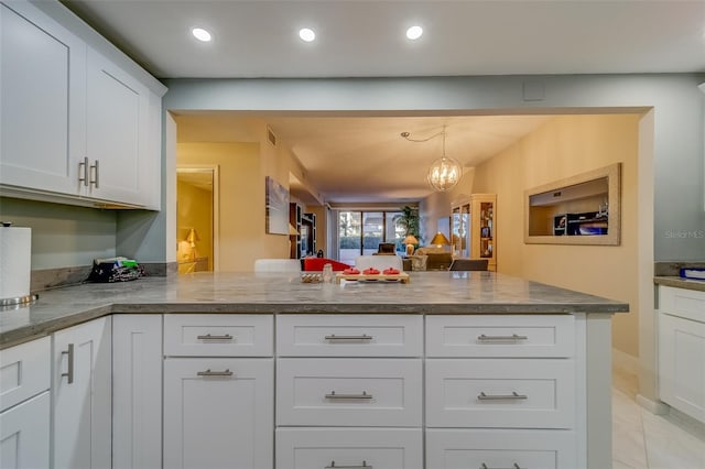 kitchen with light stone counters, a notable chandelier, kitchen peninsula, decorative light fixtures, and white cabinets