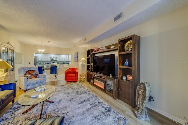 living room with a textured ceiling, light hardwood / wood-style flooring, and an inviting chandelier