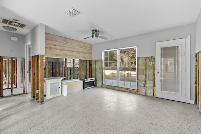 unfurnished living room with a wealth of natural light, wooden walls, and ceiling fan