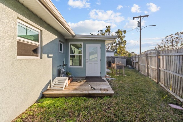 view of exterior entry featuring a lawn and a deck