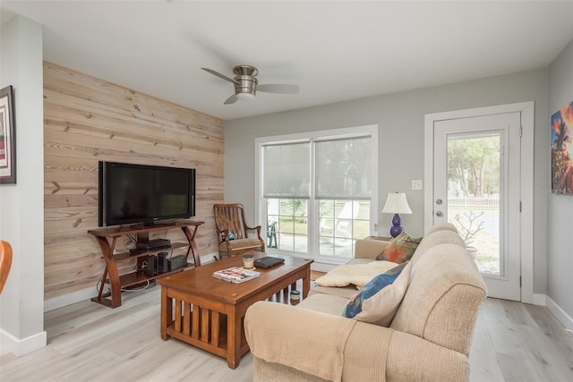 living room with ceiling fan, light wood-type flooring, and wooden walls